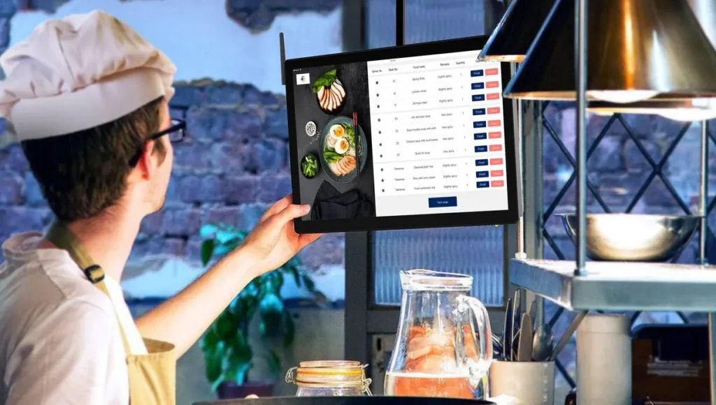 Restaurant operator reviewing menu availability on a tablet beside a busy kitchen
